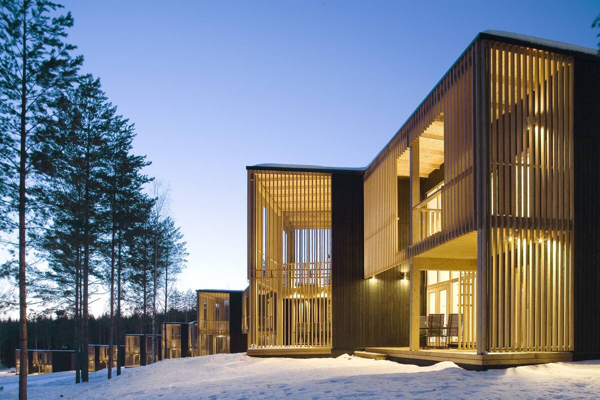 Un edificio moderno con grandes ventanales y paneles exteriores de madera, rodeado de nieve y árboles.