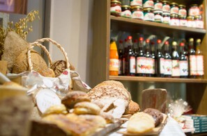 A bakery display with various breads and pastries, and a shelf of bottled beverages in the background. - Anttolanhovi (Mikkeli)