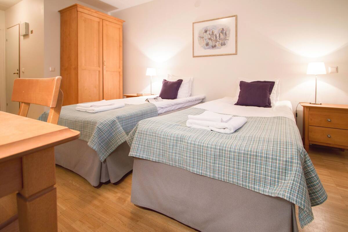 Una habitación de hotel con dos camas, un armario de madera, un escritorio y una silla.