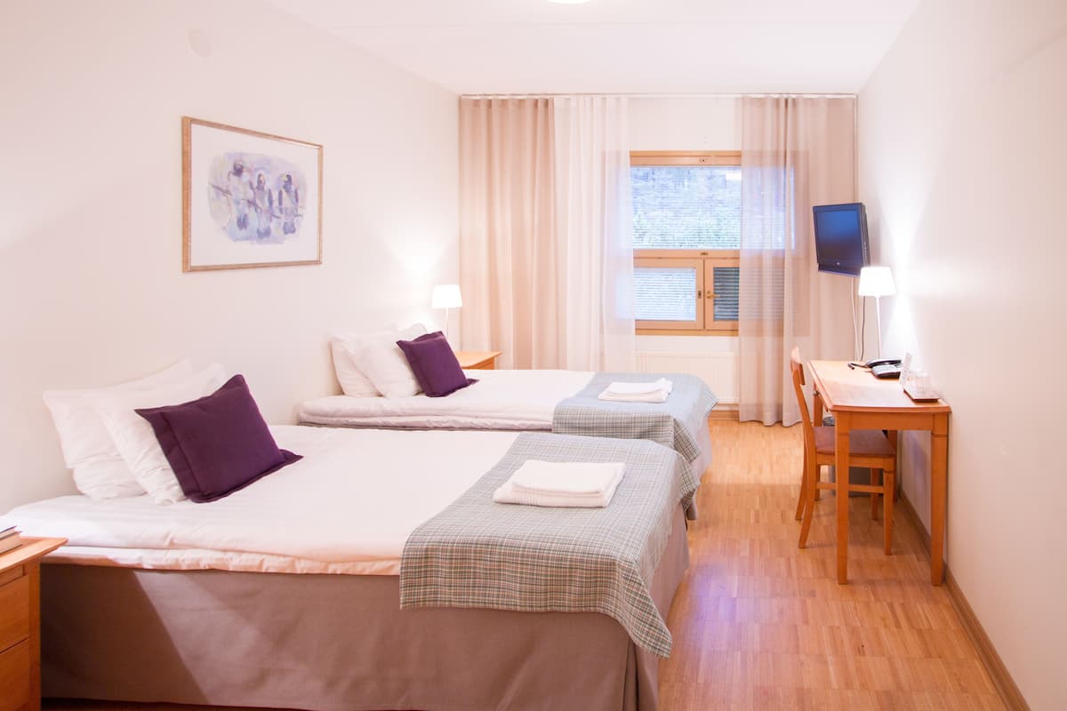 Habitación de hotel con dos camas, un escritorio, una silla, un televisor y una ventana con cortinas.