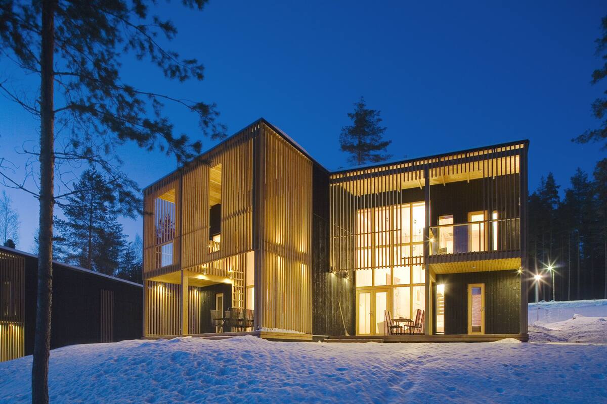 Un edificio moderno de madera con ventanas grandes y un balcón, rodeado de nieve.