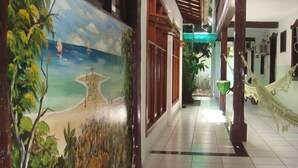 A hallway with a mural of a beach scene, a hammock, and a tiled floor. - Hotel Vale Verde (Porto Seguro)