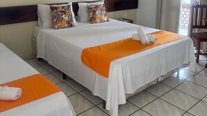 A hotel room with two beds, a large painting on the wall, an air conditioning unit, and a view of the outdoors through a window. - Hotel Vale Verde (Porto Seguro)