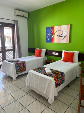 A hotel room with two beds, a green wall, a colorful abstract painting, and a window with curtains. - Hotel Vale Verde (Porto Seguro)