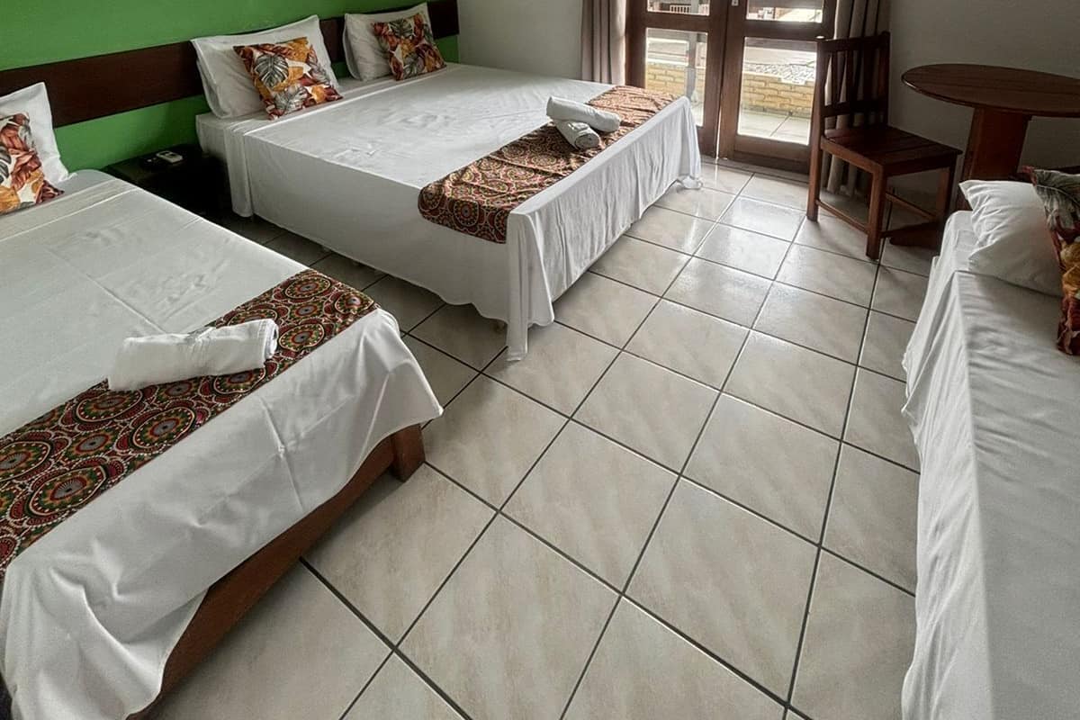 Habitació d'hotel amb tres llits, una paret verda, un quadre i vista a una població a través de la porta.
