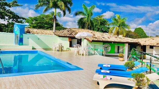 A pool area with lounge chairs and a small building with a green wall and a sign. - Hotel Vale Verde (Porto Seguro)