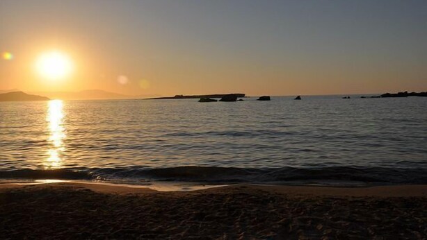 Una playa al atardecer con aguas tranquilas y formas de terreno a lo lejos.
