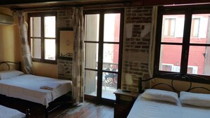 Una habitación con dos camas, piso de madera y vista a un edificio rojo a través de amplios ventanales.
