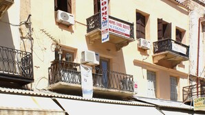 Un edificio con balcones, un cartel de alquiler y diversas tiendas en la planta baja.