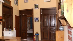 Una habitación con puertas de madera, un escritorio y una cama. Hay un extintor y un cartel que indica habitaciones disponibles.