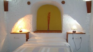 A bedroom with a bed, two bedside lamps, a vase on a shelf, and a wall-mounted power outlet.
