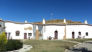 Edifici blanc amb diverses portes i finestres, mur de pedra i una petita zona de jardí amb un camí.