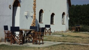 A building with a white exterior, multiple windows, and a table with chairs in front.