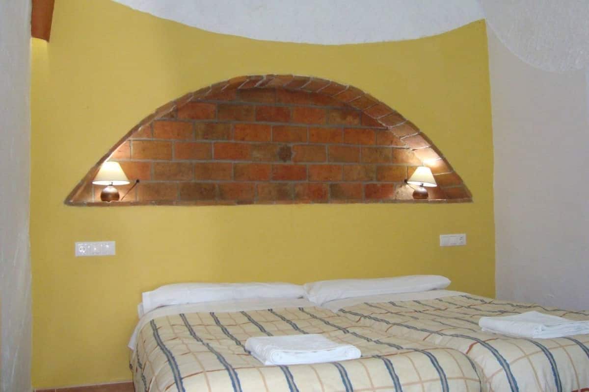 A room with a bed, yellow walls, and a brick fireplace with two wall-mounted lamps.