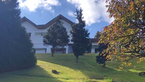 Um edifício com fachada branca e telhado inclinado, rodeado por árvores e um gramado.