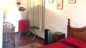 Um quarto com uma cama, um armário vermelho, uma cadeira de madeira, uma mesa pequena e um aquecedor.