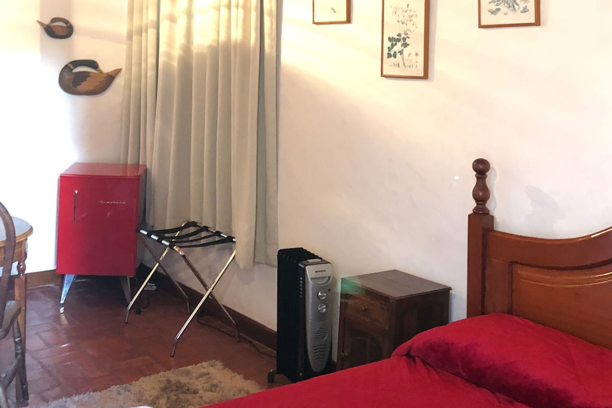 Une chambre à coucher avec un lit, une armoire rouge, une chaise en bois, une petite table et un radiateur.