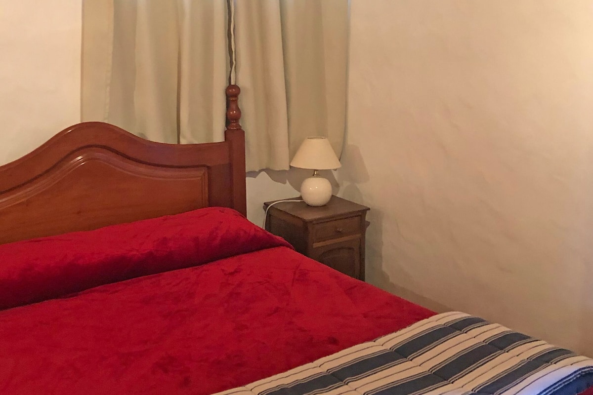 Un lit simple avec une tête de lit en bois, une couvre-lit rouge, une lampe de chevet et une table de chevet.