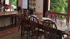 Uma área de refeições com uma mesa e cadeiras de madeira, um vaso com frutas e vista para o verde lá fora.