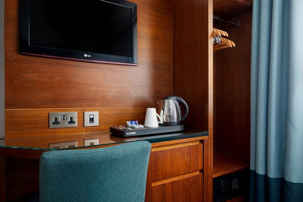 A hotel room with a wooden desk, a television, a coffee maker, and a coat rack.
