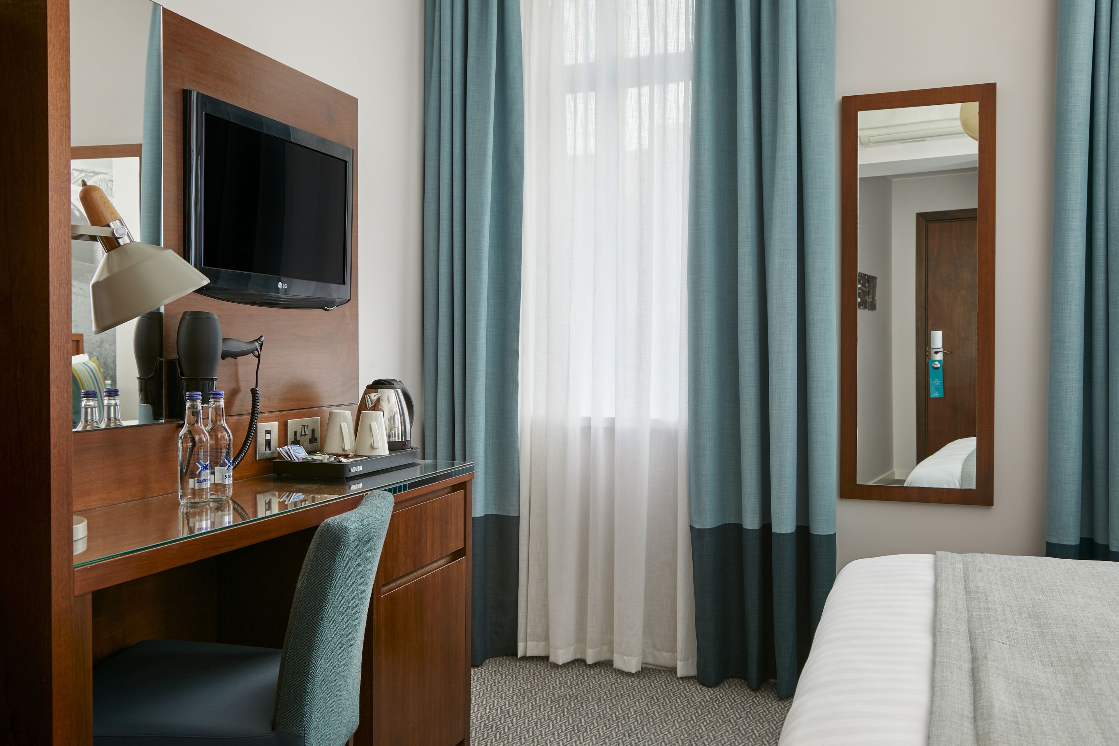 A hotel room with a wooden desk, a flat-screen TV, a mirror, and a bed.