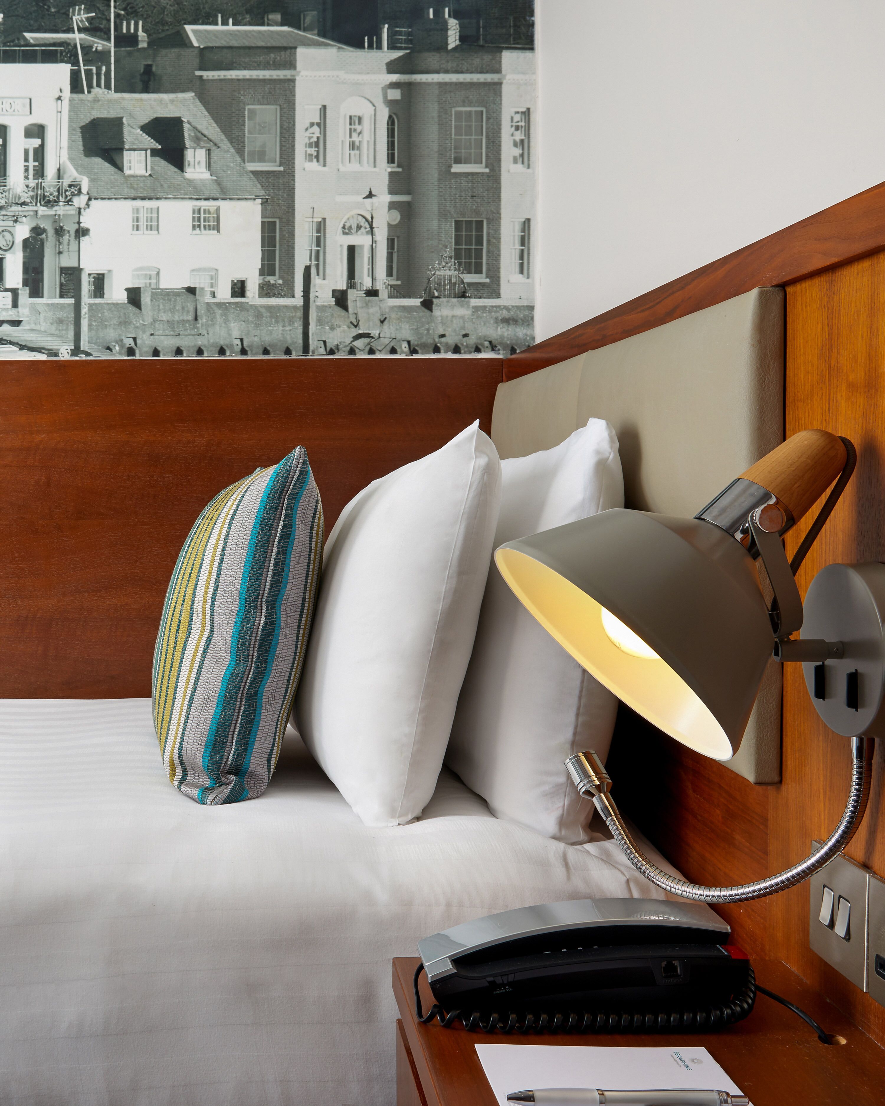 A hotel room with a bed, a lamp, a telephone, and a view of buildings through a window.