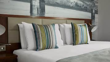 A hotel room with a large bed, striped pillows, a headboard, a nightstand, a lamp, and a wall mural of a bridge over water.