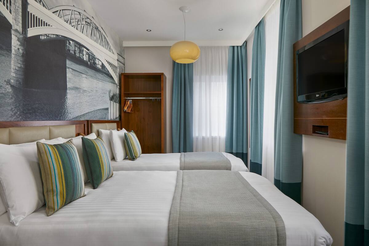 A hotel room with two beds, a large painting of a bridge, a television, and a wardrobe.