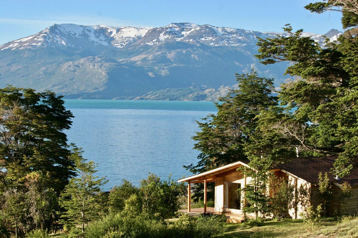 A cabin with a wooden deck overlooking a lake and mountains.