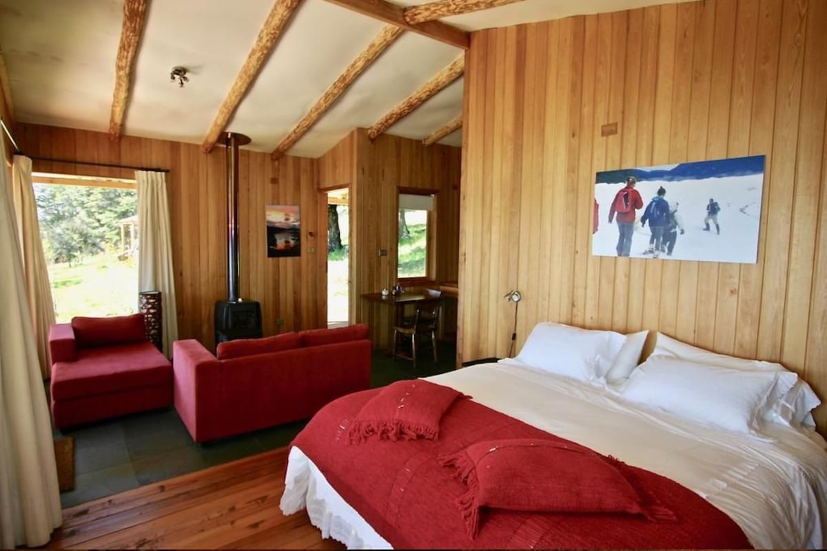 Un interior de madera con una cama, sofás rojos, un televisor y un cuadro en la pared.