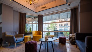 A modern lounge area with a sofa, armchairs, ottomans, a coffee table, and large windows offering a city view. - First Hotel Amalie (Tromsø)