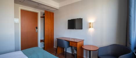 A hotel room with a bed, a desk, a chair, a television, and a small table.