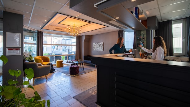 A modern hotel lobby with a reception desk, seating area, and large windows offering views of the city. - First Hotel Amalie (Tromsø)