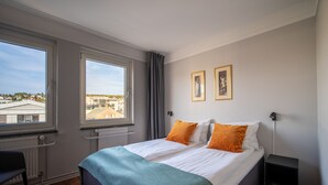 A hotel room with a bed, two windows, a chair, and a nightstand. - First Hotel Amalie (Tromsø)
