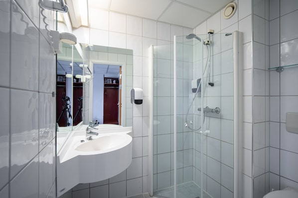 Un baño moderno con ducha envuelta en vidrio, un lavabo blanco y un espejo grande.