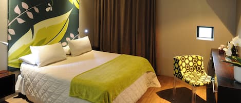 A hotel room with a large bed, a chair, a desk, and a TV on the wall.