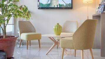 Una habitación con una mesa redonda, dos sillas estampadas, un jarrón verde, una planta en maceta y un cuadro en la pared.