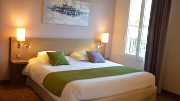 Habitación de hotel con una cama grande, dos lámparas de noche, un cuadro en la pared y una ventana con cortinas.