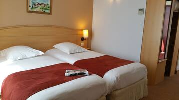 A double bed with white and red bedding, a nightstand with a lamp, and a painting on the wall.