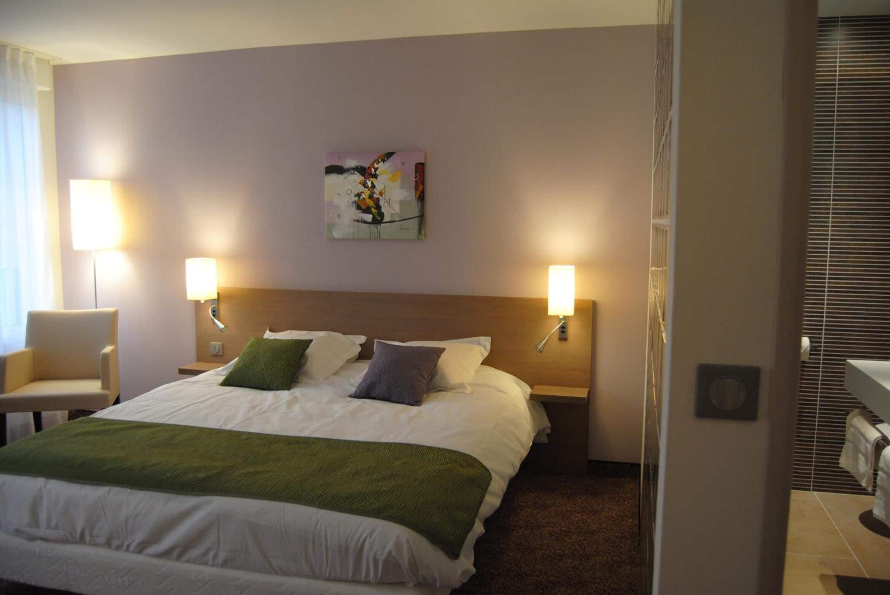 Una habitación de hotel con una cama grande, dos lámparas de noche, un cuadro en la pared y una silla.