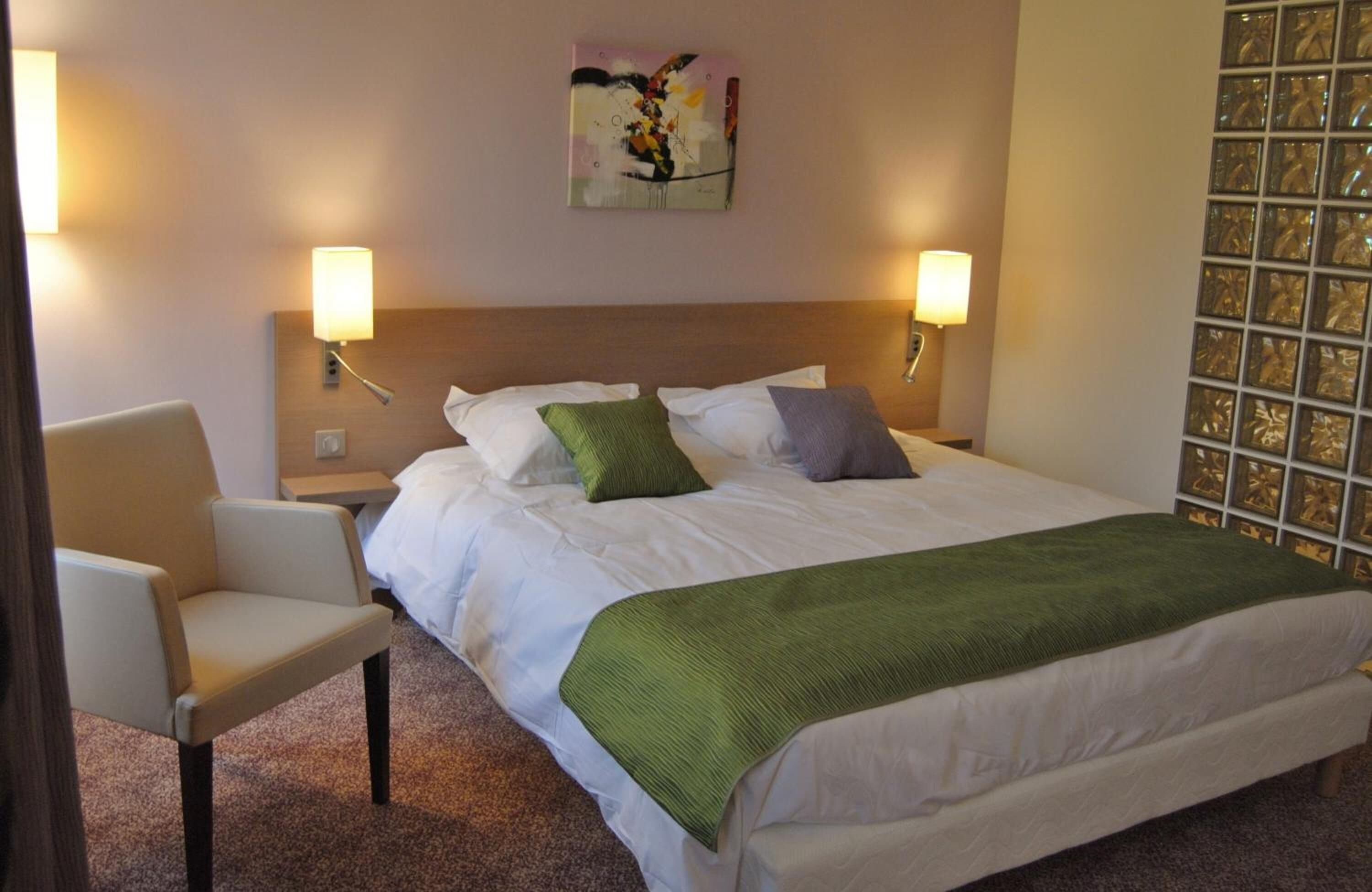 Une chambre d’hôtel comprenant un lit, deux lampes de chevet, une chaise et un élément décoratif mural.
