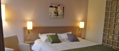 Una habitación de hotel con una cama, dos lámparas de noche, una silla y un adorno en la pared.