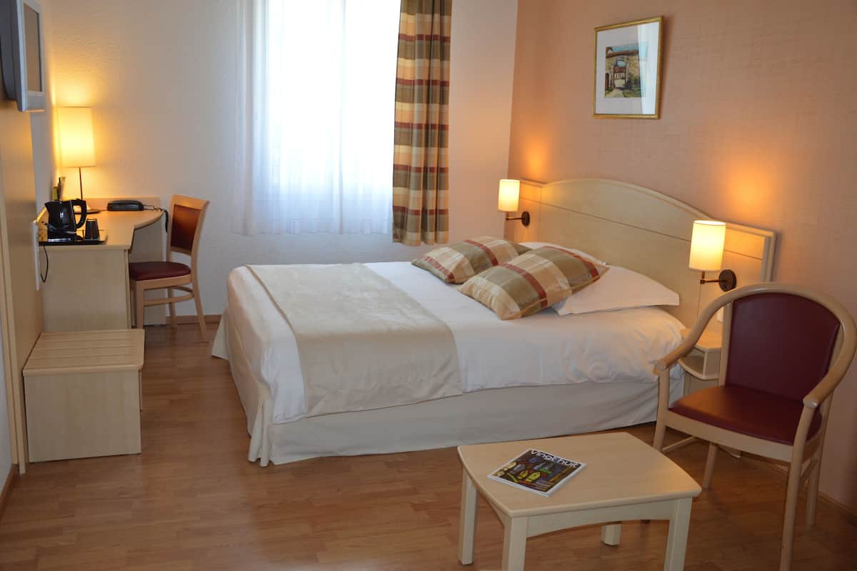 A hotel room with a bed, a desk, a chair, a table, and a lamp.