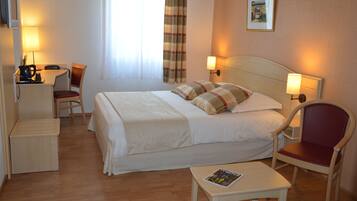 A hotel room with a bed, a desk, a chair, a table, and a lamp.