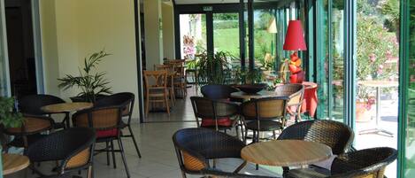 Un patio interior con sillas y mesas de mimbre, una puerta de cristal que da al exterior y una lámpara roja.