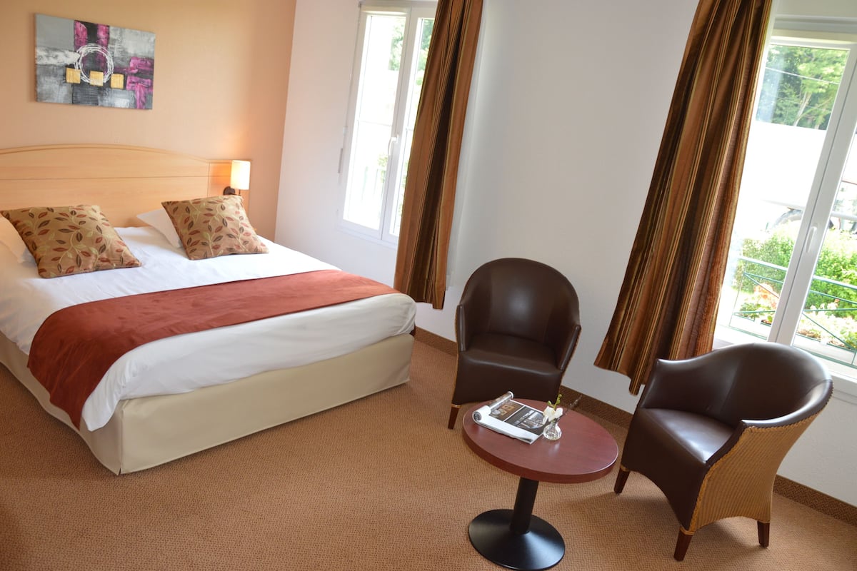 A hotel room with a bed, two chairs, a small table, and a window with curtains.