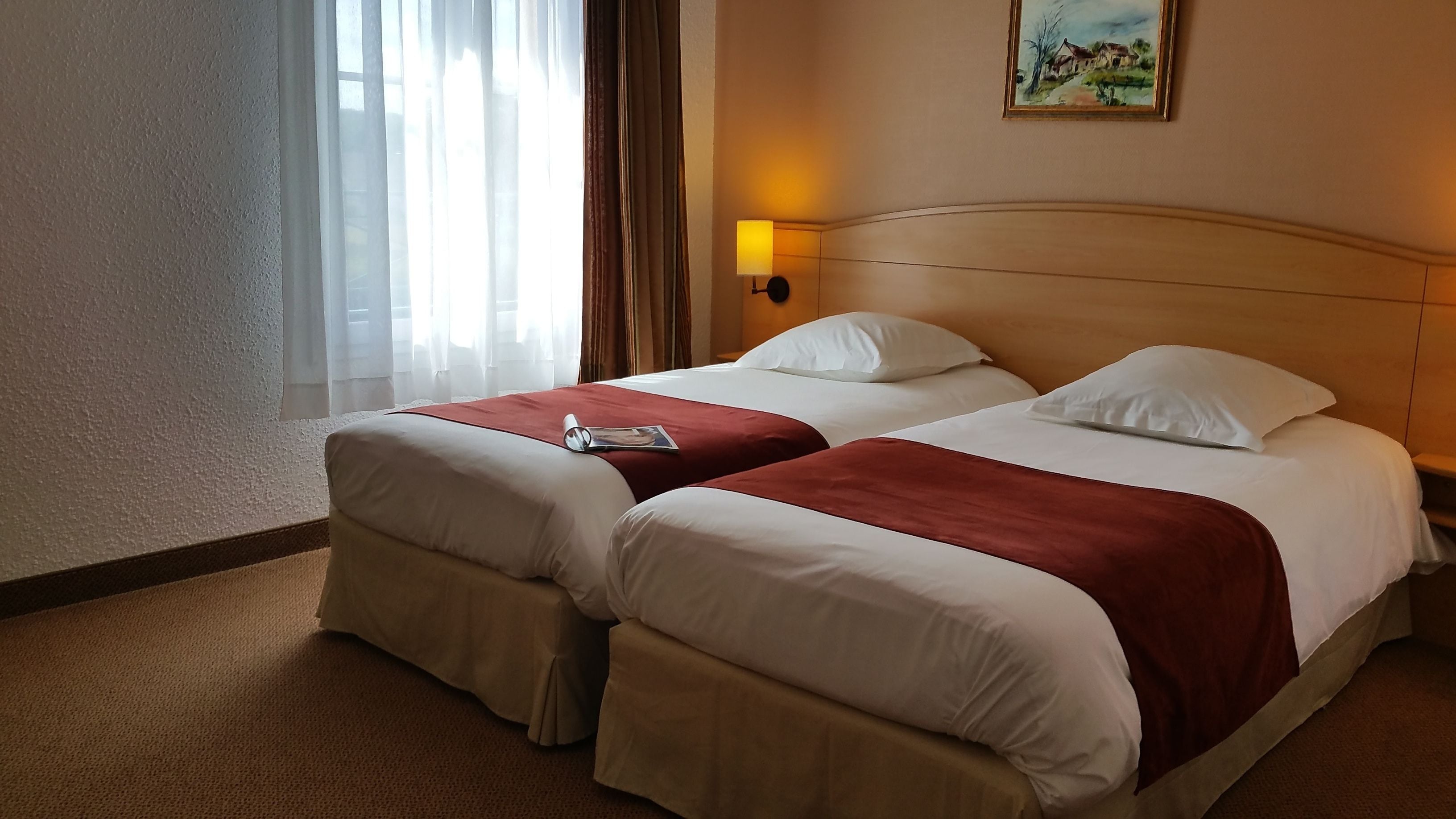 Una habitación de hotel con dos camas, una mesita de noche, una lámpara y un cuadro en la pared.