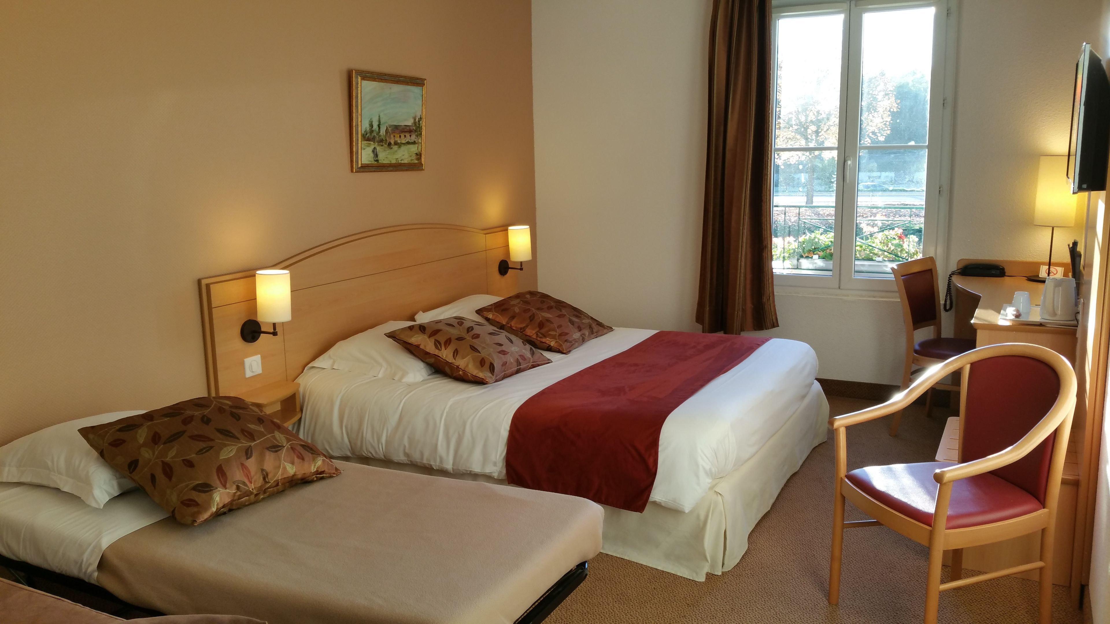 A hotel room with two beds, a desk with a chair, a TV, and a window with curtains.