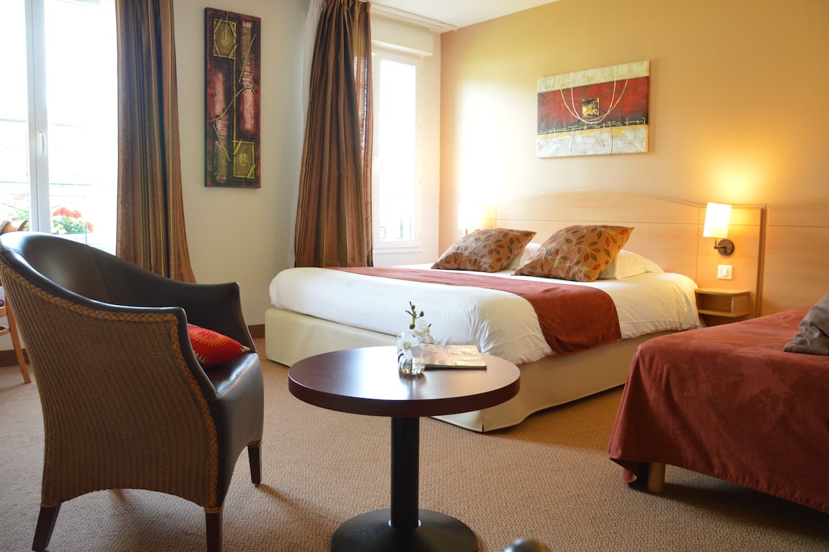 A hotel room with a bed, a chair, a table, and a painting on the wall.