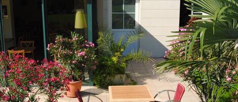A building with a covered patio, potted plants, and a table with chairs.